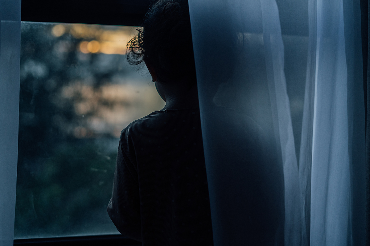 View of a young child looking out a window in the dark